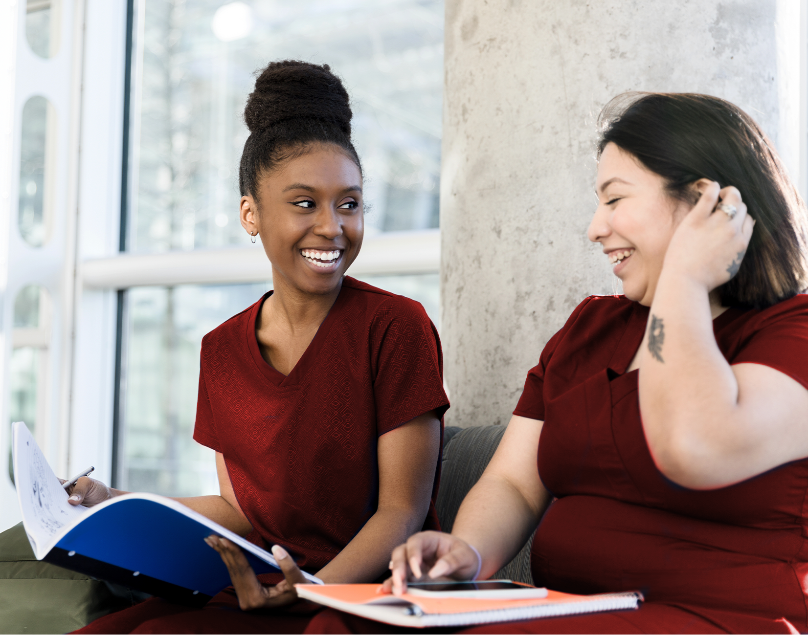 Duas profissionais de odontologia sorridentes em uniforme bordô conversando, simbolizando colaboração acadêmica e bem-estar no ambiente de trabalho.