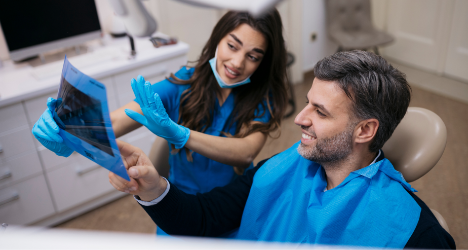 Dentista de uniforme azul mostra radiografia panorâmica para paciente sorridente em consulta odontológica de rotina e diagnóstico.