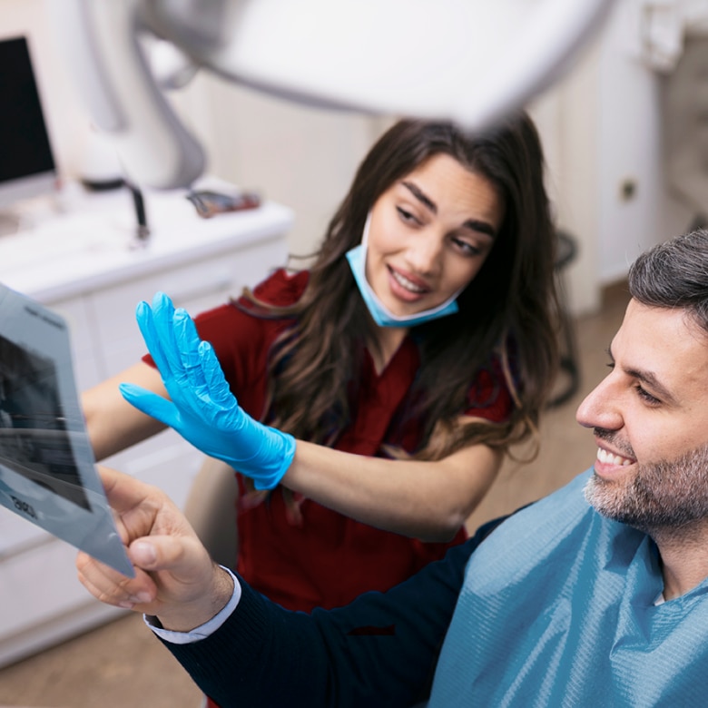 Dentista explicando radiografia panorâmica para paciente sorridente em consultório odontológico moderno com foco em diagnóstico e saúde bucal.