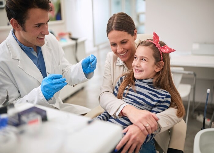 Dentista realizando atendimento em uma criança, acompanhada de sua mãe