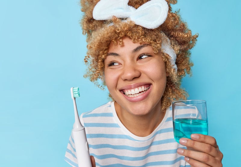 mulher utilizando escova de dente elétrica e enxaguante bucal